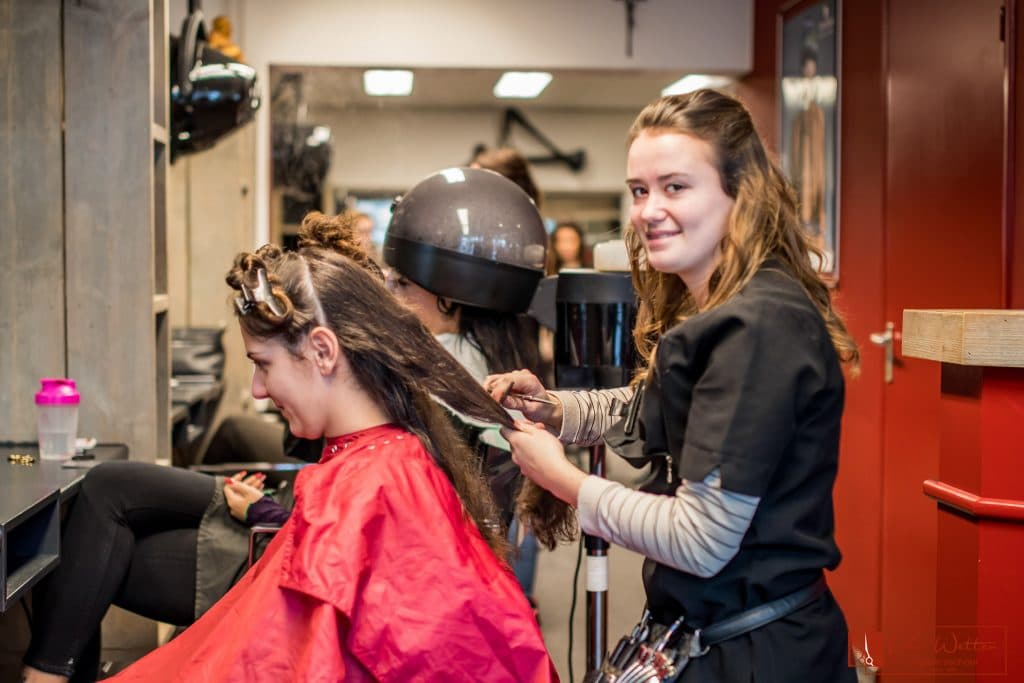 Docent begeleidt een leerling bij het knippen in de kappersschool