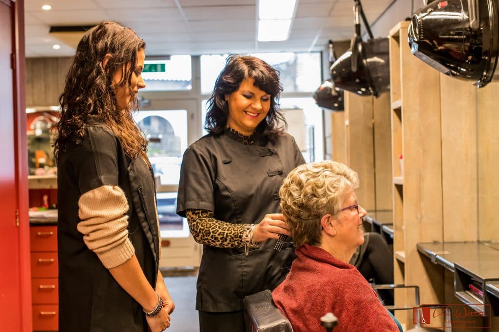 Leerling knipt het haar van een klant in de kapsalon van Van Wetten